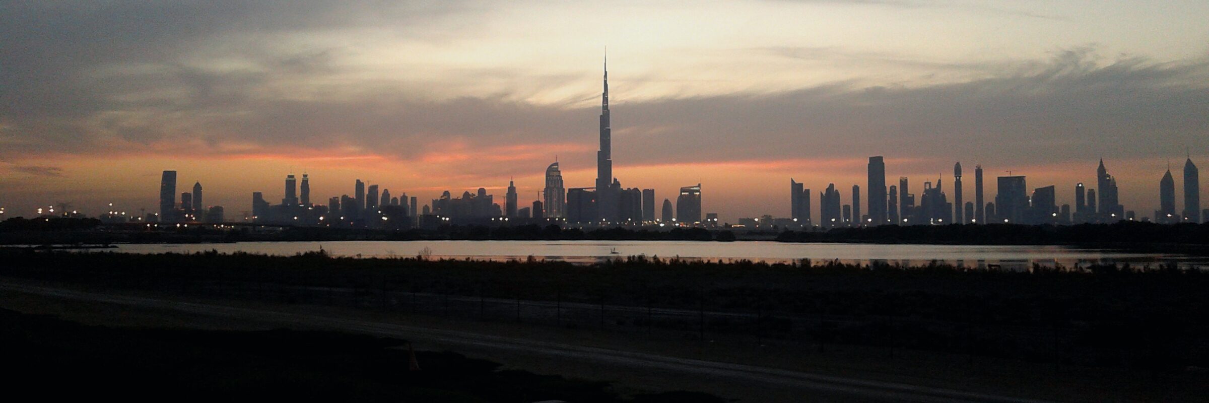 The Dubai skyline in silhouette at sunset, with the Burj Khalifa at its centre